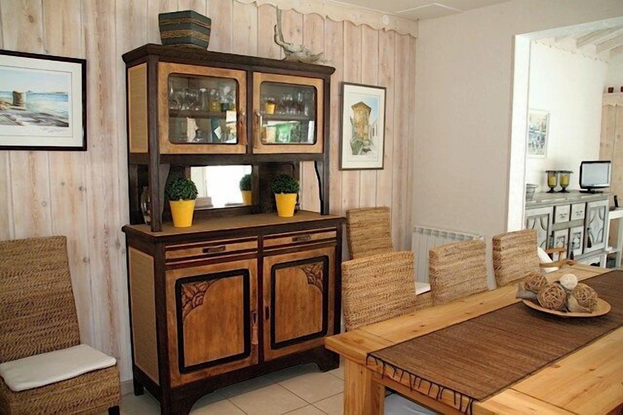 A dining area with a wooden table and chairs, a cabinet with glass doors, and wicker chairs.