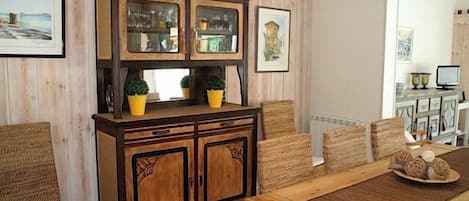 A dining area with a wooden table and chairs, a cabinet with glass doors, and wicker chairs.