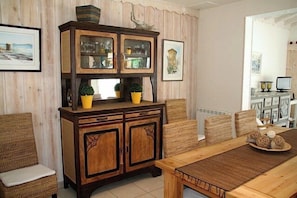 Een eetgedeelte met een houten tafel en stoelen, een kast met glazen deuren, en rieten stoelen.