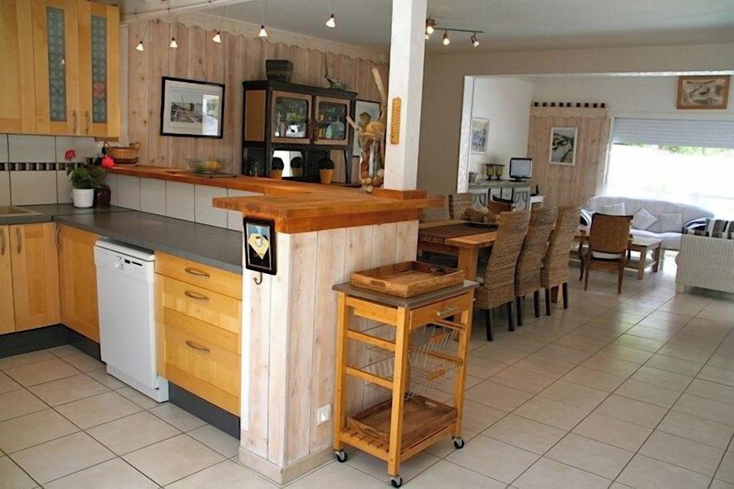 Une cuisine avec des meubles en bois, un lave-vaisselle et un coin repas comprenant des chaises et une table.