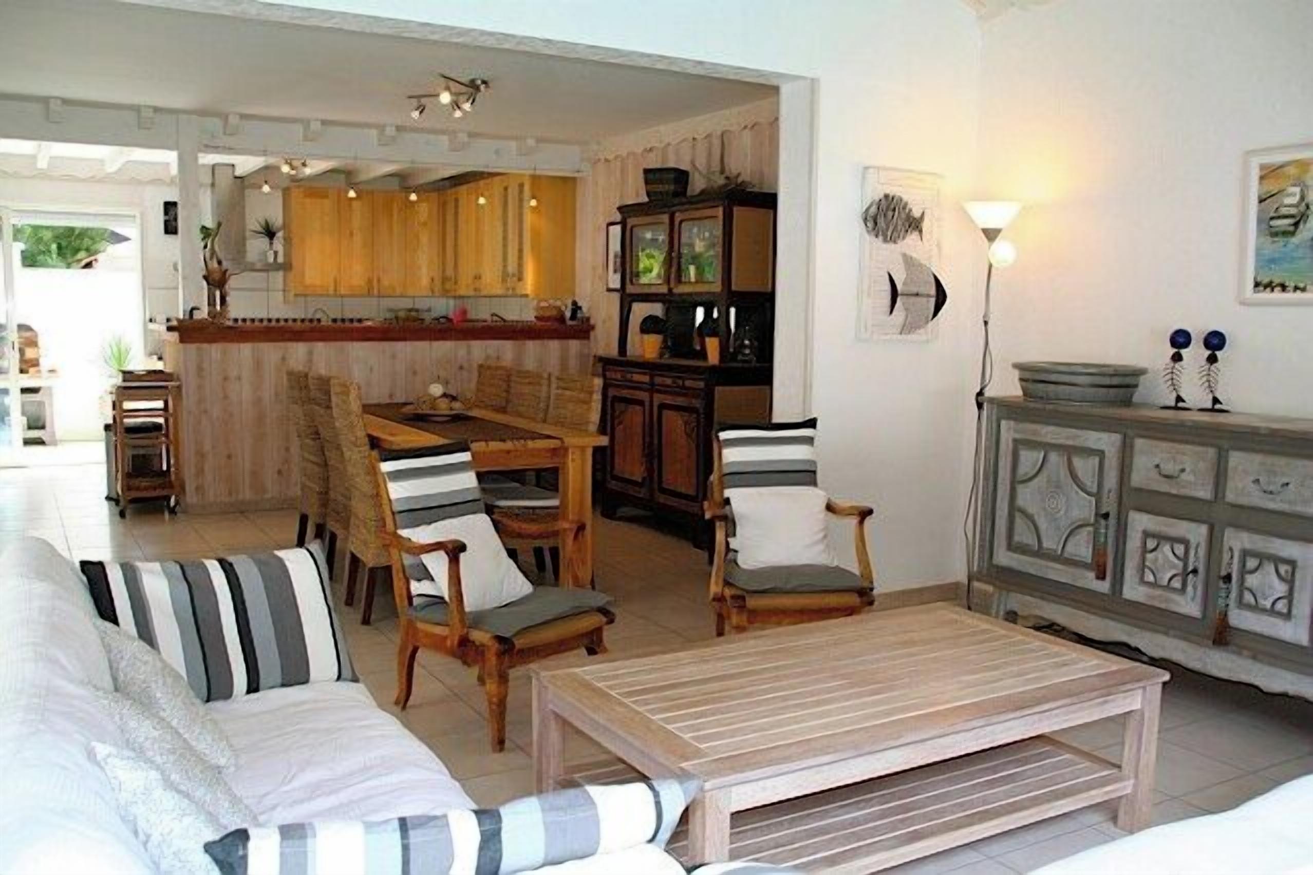 A living room with a sofa, chairs, a dining table, and a kitchen area in the background.