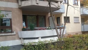 Un immeuble résidentiel à plusieurs étages, doté de balcons, d’un petit jardin et d’une allée pavée.