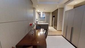 Una cocina moderna con una isla central, un comedor con mesa y sillas de madera, y un pasillo que lleva a un dormitorio.