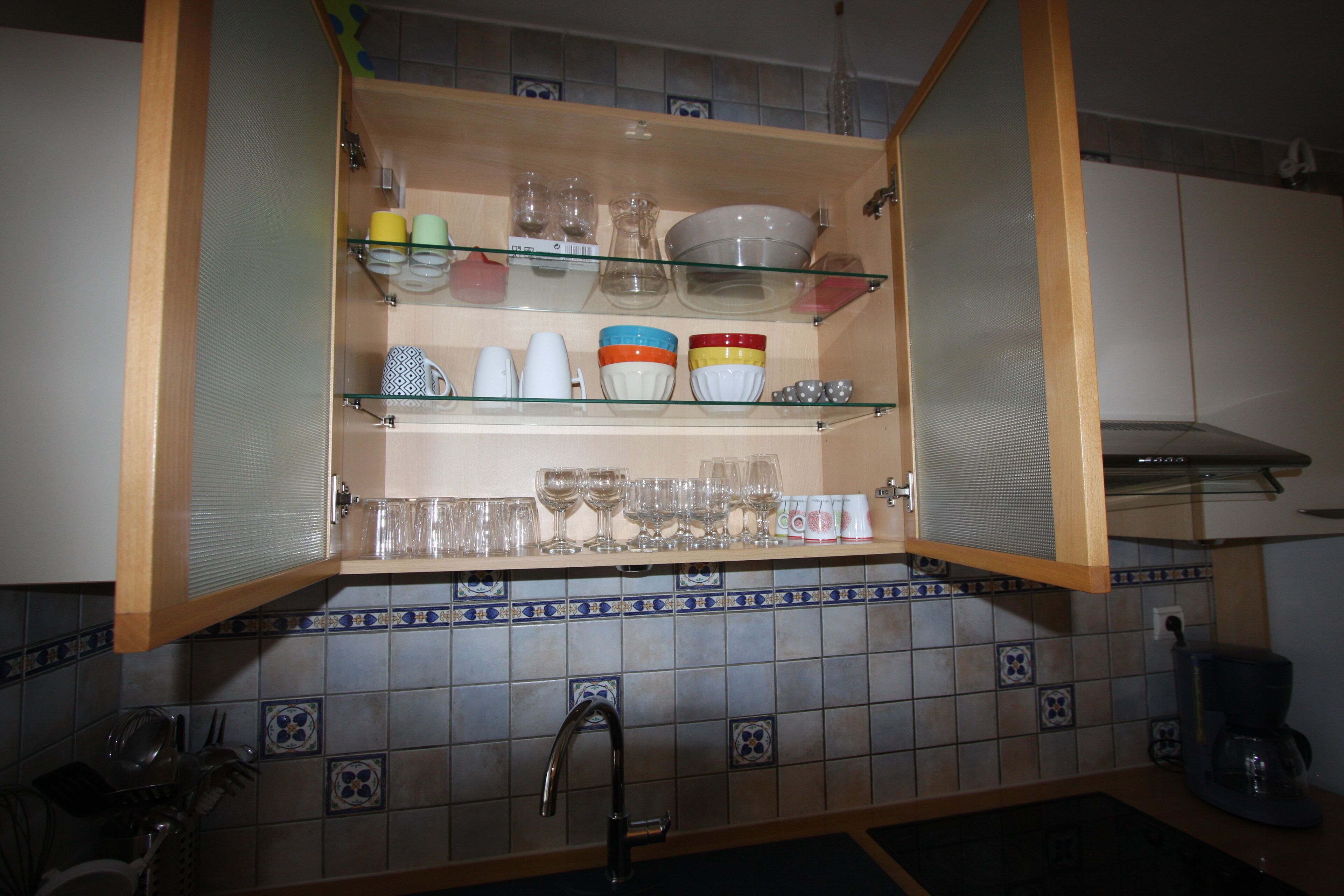 An open kitchen cabinet with shelves holding various glassware and dishes.