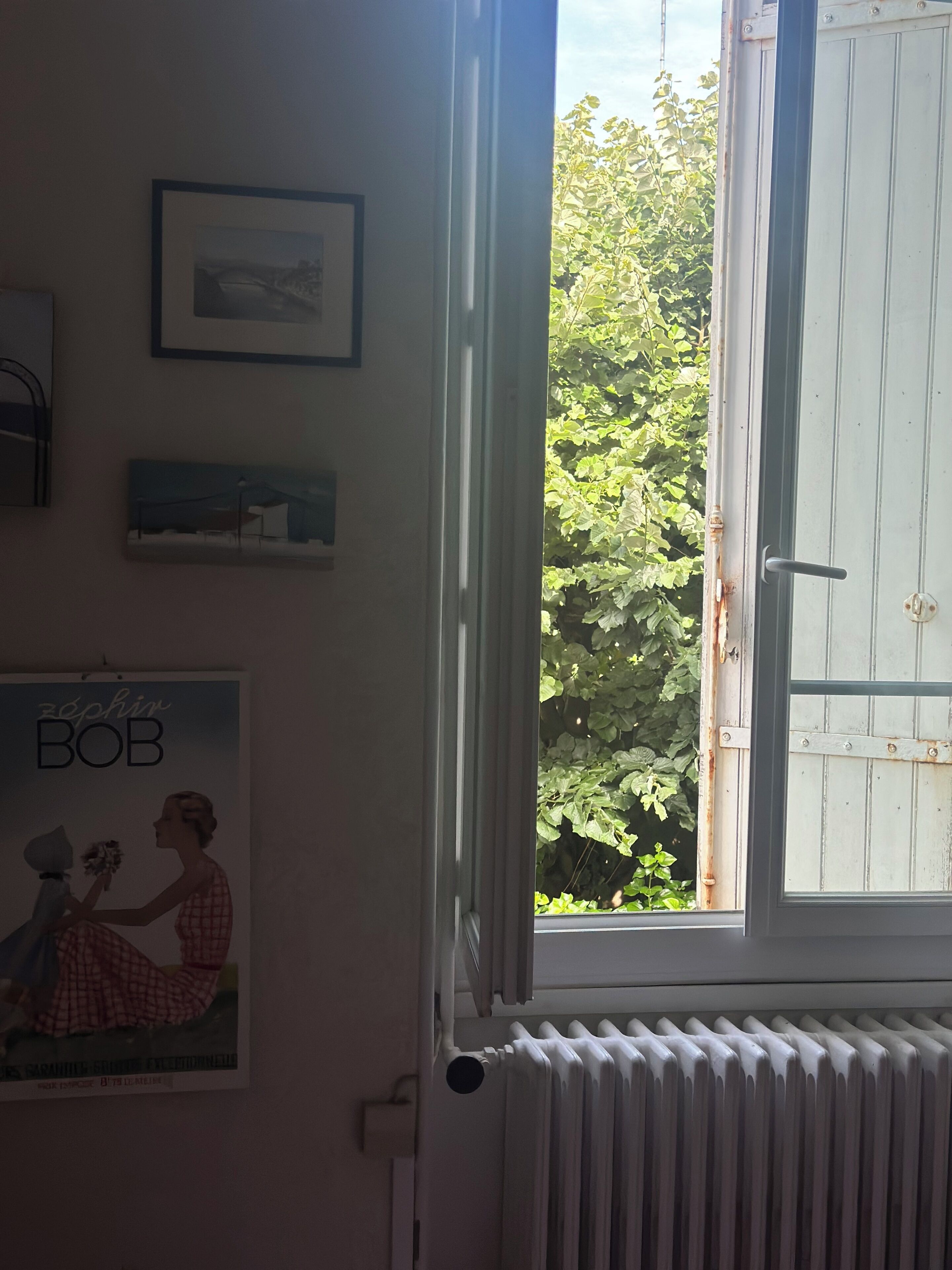 Ein Zimmer mit Fenster, Heizkörper und einem Poster an der Wand.