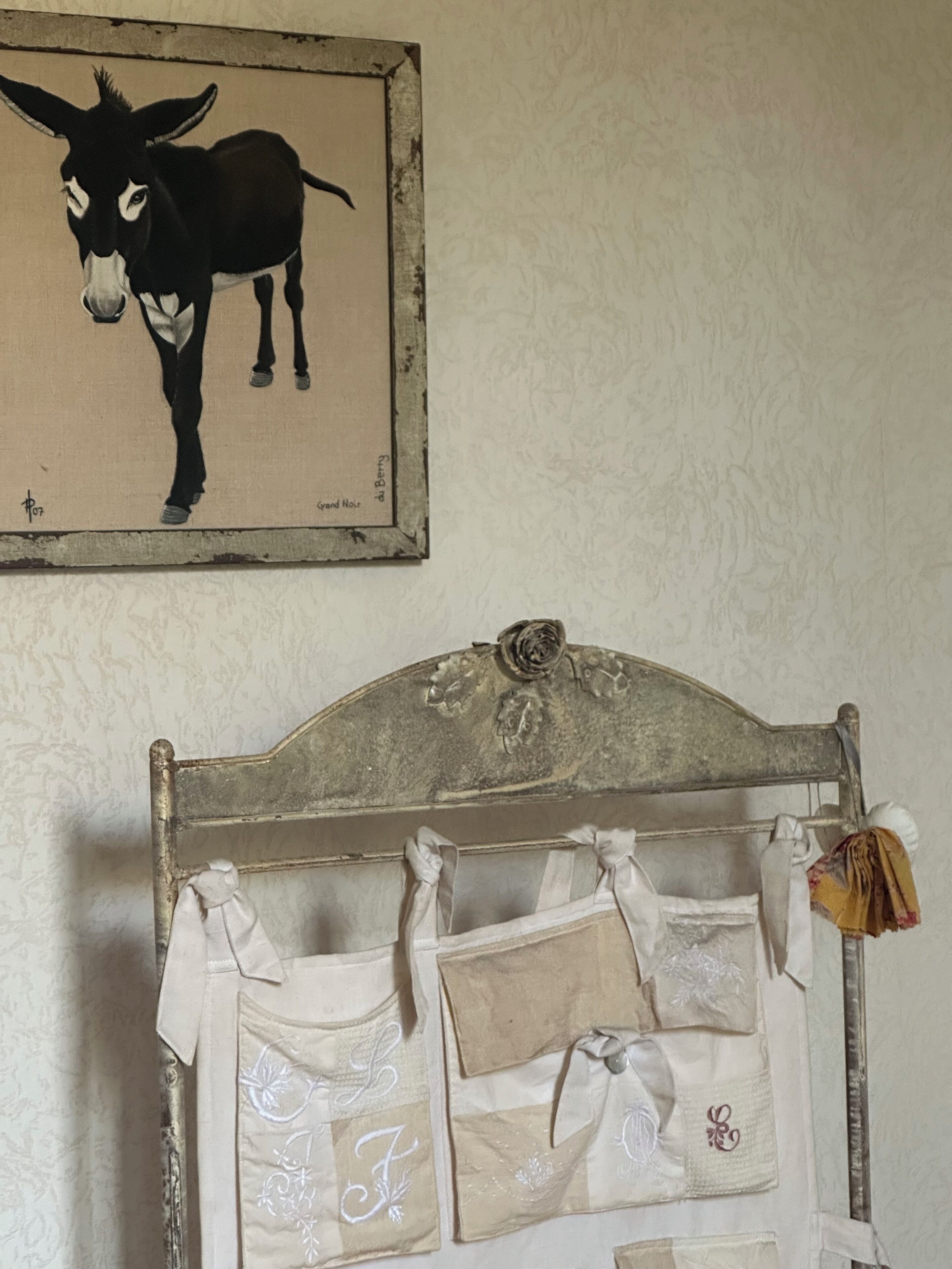 A rustic bed frame with a decorative headboard, a wall-mounted painting of a donkey, and a bed with multiple pillows and a folded blanket.