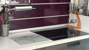 A kitchen with a dark maroon backsplash, a stainless steel range hood, and a stainless steel sink. There is a metal utensil holder with various kitchen tools and a placemat with the text "Cuisine Royale Paris." - STANDING APARTMENT IN THE CENTER OF LA ROCHELLE 2 STEPS FROM THE OLD PORT AND BEACH (La Rochelle)