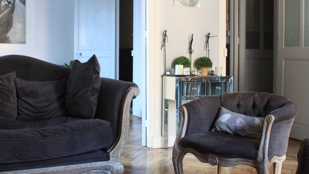 A living room with a dark-colored sofa and armchair, a small side table with decorative items, and a door leading to another room. - STANDING APARTMENT IN THE CENTER OF LA ROCHELLE 2 STEPS FROM THE OLD PORT AND BEACH (La Rochelle)