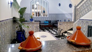 Un interior marroquí con suelo a cuadros, paredes con estampado azul y blanco, una escalera y un espejo grande que refleja una habitación con cama y ventana.