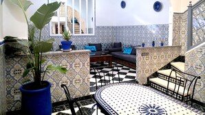 Un interior al estilo marroquí con suelo a cuadros, paredes con motivos, un sofá azul y un comedor con mesa y sillas.