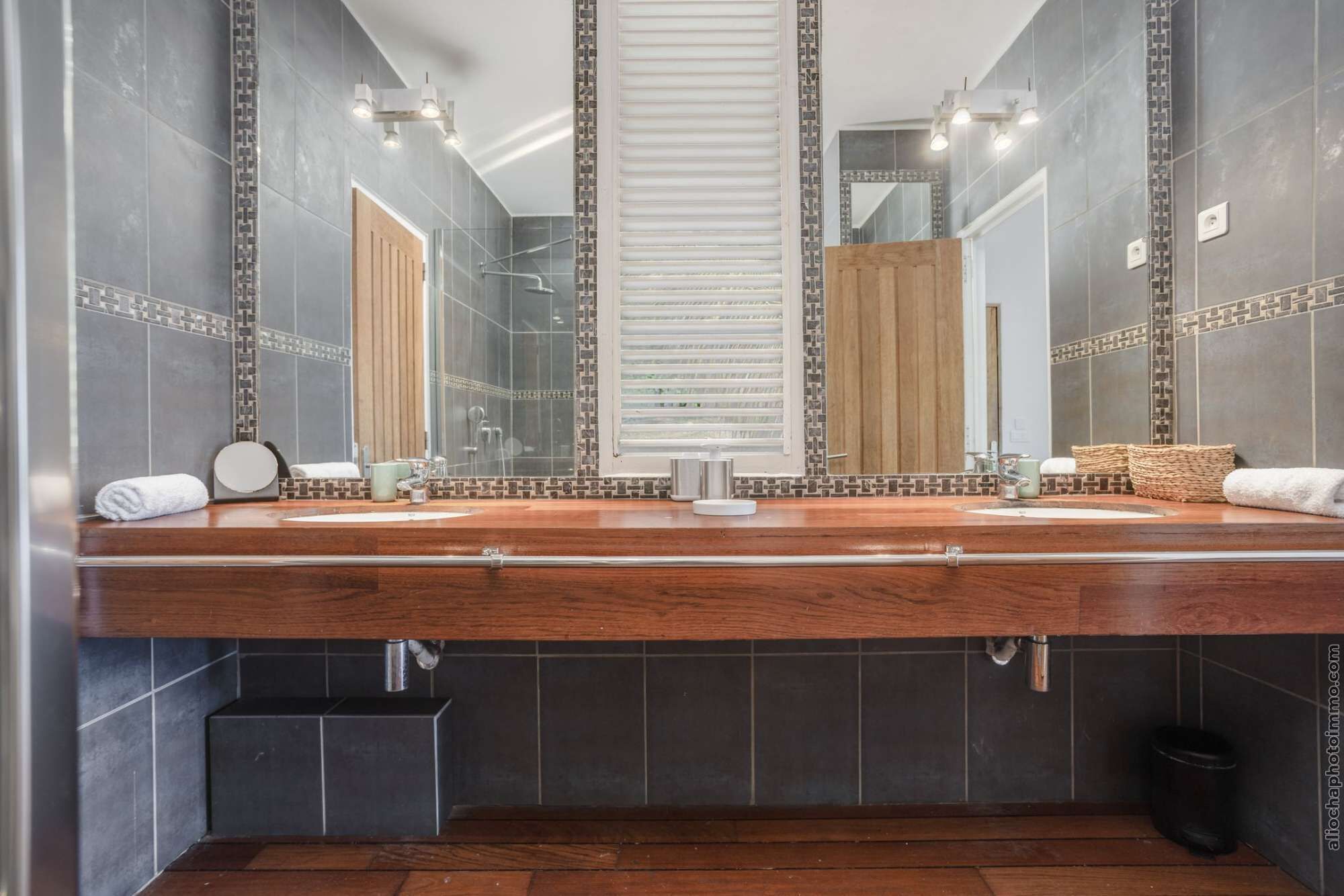 A modern bathroom with a wooden vanity, large mirrors, and a shower area.