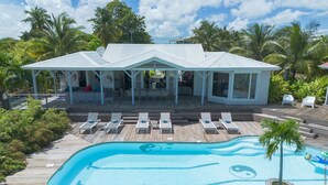 Un resort con piscina que presenta un diseño de yin-yang, sillas de descanso y una zona de estar techada con vista a la piscina.