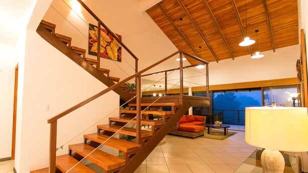 Amplia sala de estar con una escalera de madera, un sofá y una lámpara.