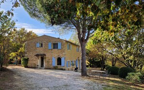 A stone house with a gravel driveway, a dining table, and chairs outside. - The Gîte (Bonnieux)