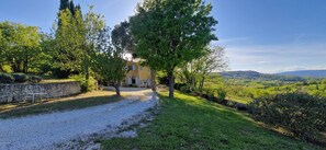 Une maison avec une allée en gravier, entourée d’arbres et d’un mur de pierres.