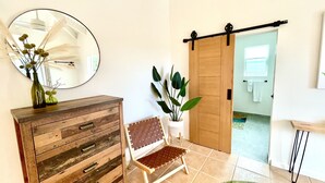 Ein Zimmer mit einem Holzkasten, einem Stuhl, einem großen Spiegel und einer Schiebetür zu einem weiteren Raum.