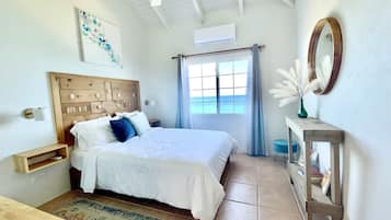 A bedroom with a wooden headboard, a bed with white bedding, a window with blue curtains, a mirror, and a small table with a vase.