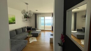 Een moderne woonkamer met een grijze bank, een klein rond tafeltje met een vaas, en een grote spiegel.