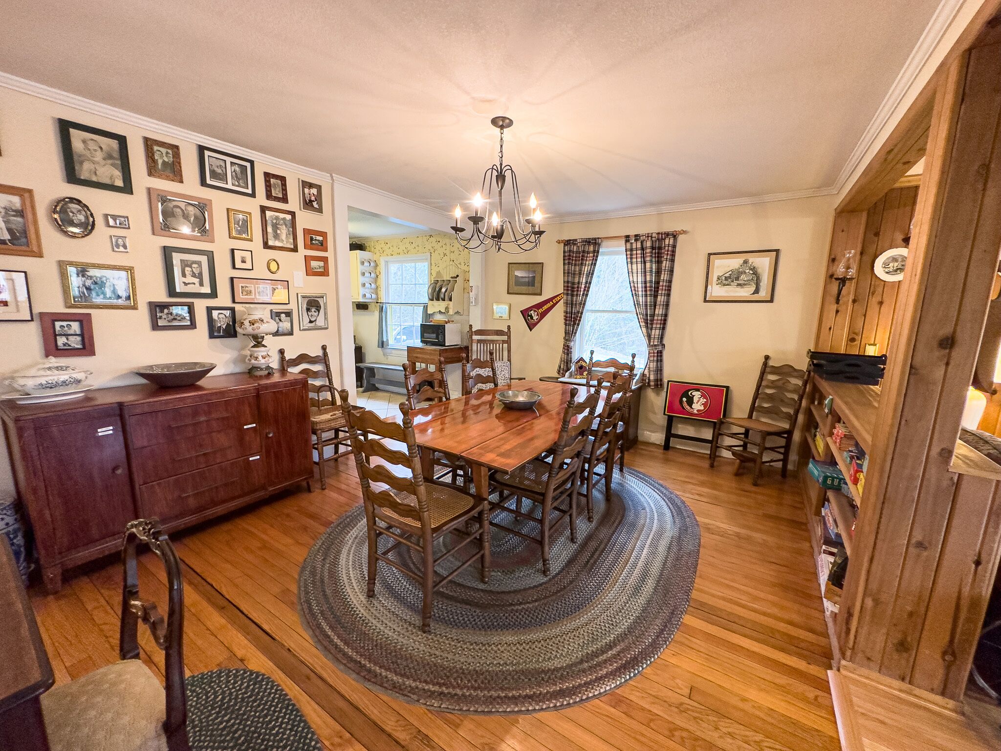 A dining room with a wooden table, chairs, a chandelier, and a wall adorned with framed photographs.