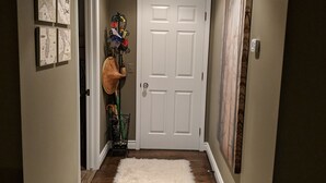 A hallway with a white door, a white shag rug, and wall-mounted artwork.