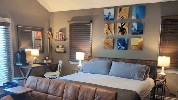 A bedroom with a bed, a leather sofa, a desk, and a nightstand with lamps.