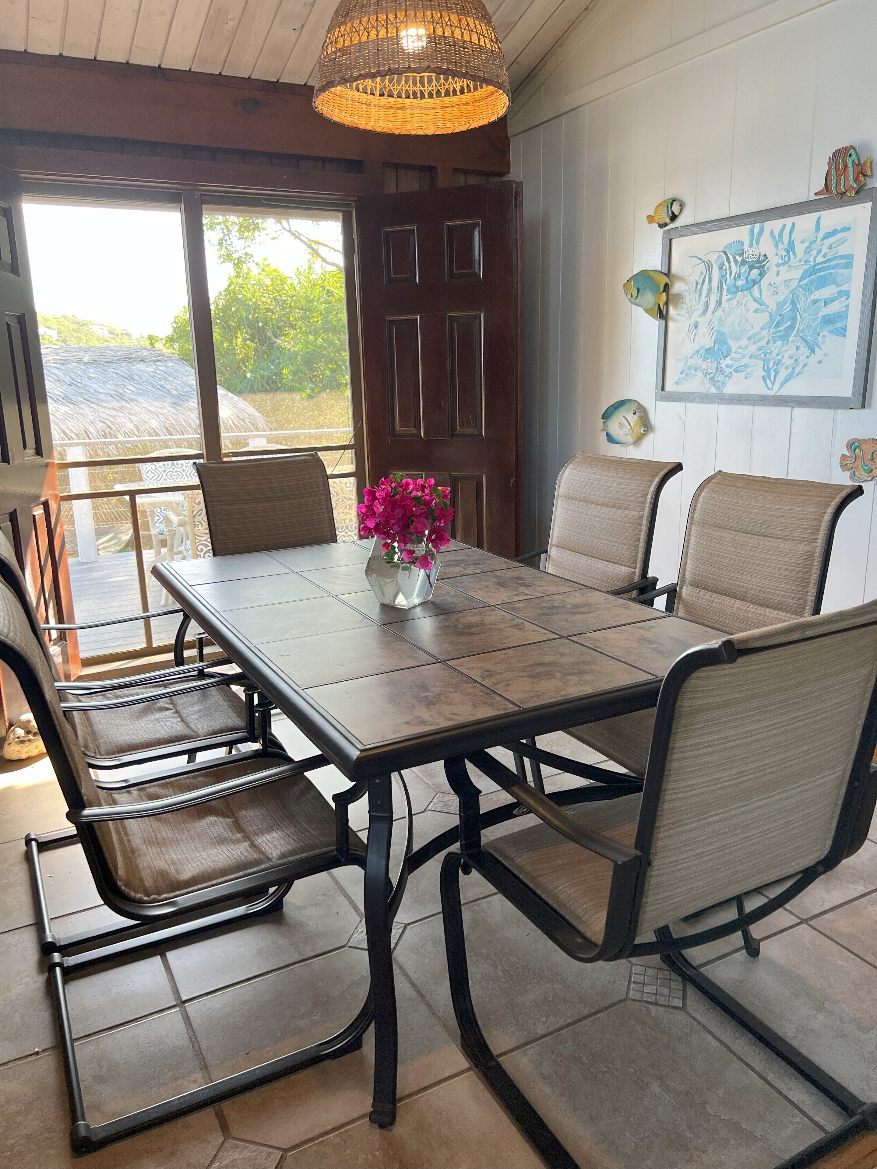 A dining area with a wooden table, cushioned chairs, a decorative hanging light, and a framed marine life painting on the wall.