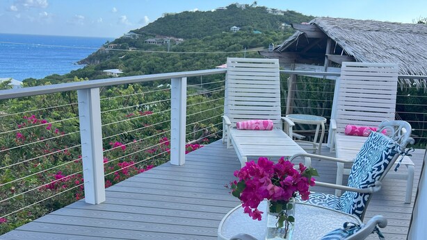 Una terraza con muebles de exterior, una mesa con un jarrón de flores y vistas al océano y las colinas.