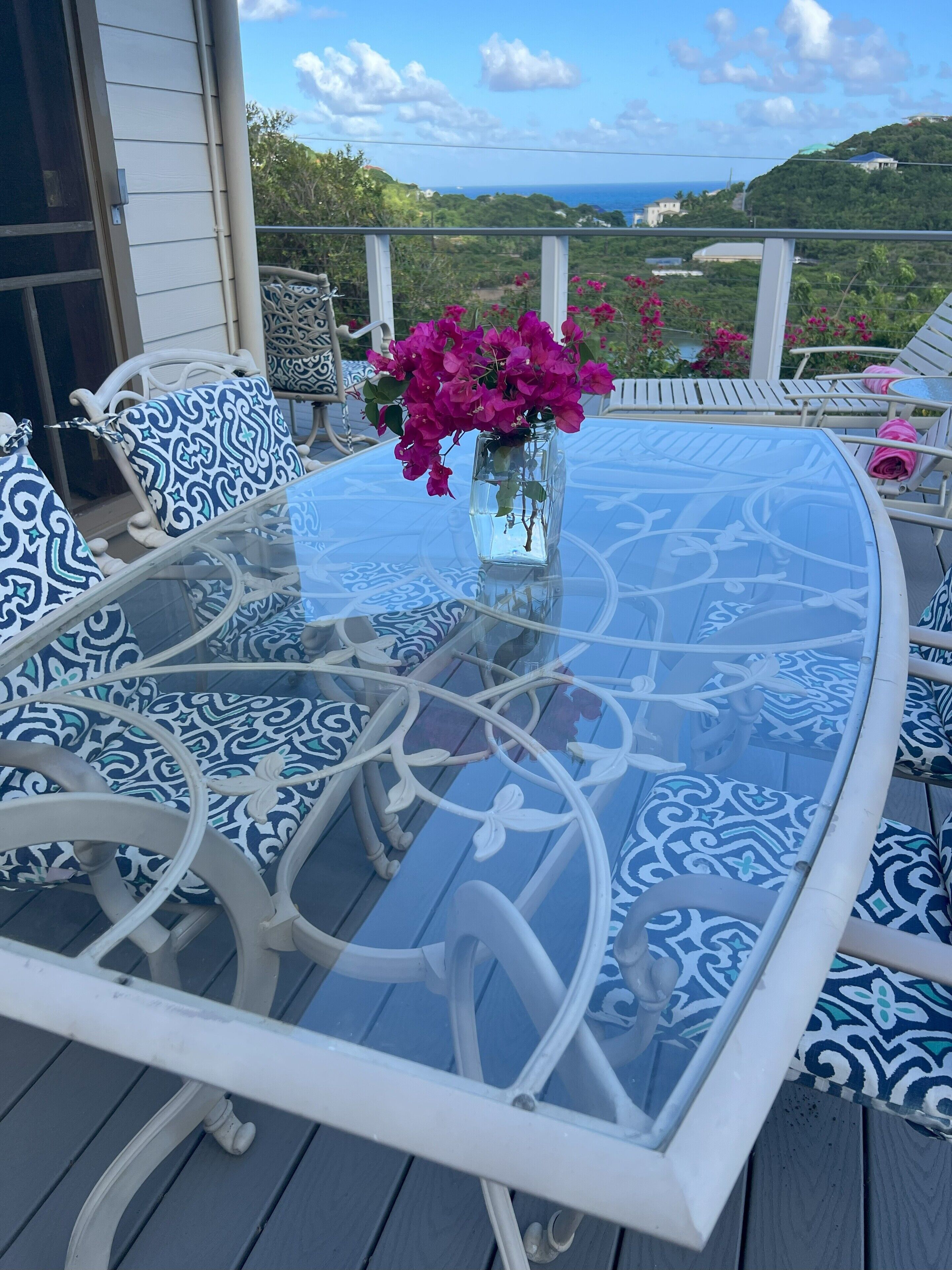 Ein Tisch mit Glasplatte, blaue Kissen mit Muster und ein Blick auf eine Küstenlandschaft.