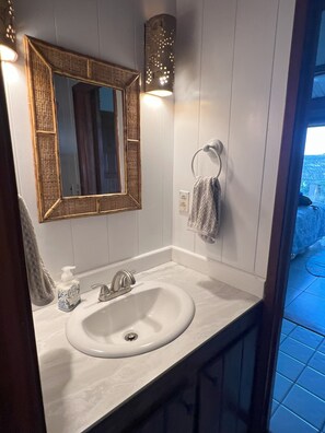 A bathroom with a white sink, a mirror with a wooden frame, a towel ring, and a wall-mounted light fixture.