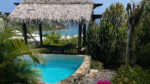 Un área junto a la piscina con sillones de descanso, techo de paja y vista al océano.