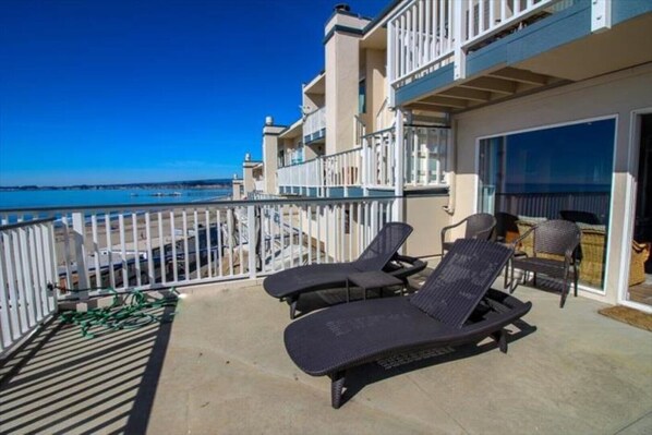 A balcony with two lounge chairs and a table, overlooking a beach and the sea.