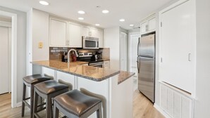 Una cocina moderna con armarios blancos, encimera de granito, electrodomésticos de acero inoxidable y una isla central con taburetes de bar.