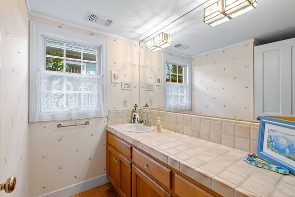 A bathroom with a sink, mirror, and window with lace curtains. - Vacation Home in Seabright (Santa Cruz)