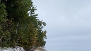 A rocky beach with large boulders and a line of trees. - Charlevoix Cottage: 150ft Lake Michigan Beach, Spectacular Sunsets & Dark Skies. (Charlevoix)