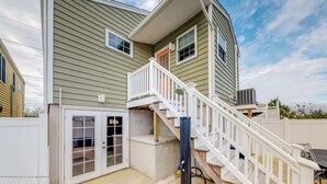 Ein zweistöckiges Haus mit einer überdachten Terrasse und einer weißen Treppe, die zu der oberen Etage führt.