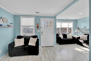 A living room with two black sofas, a white door, and a window with blinds.