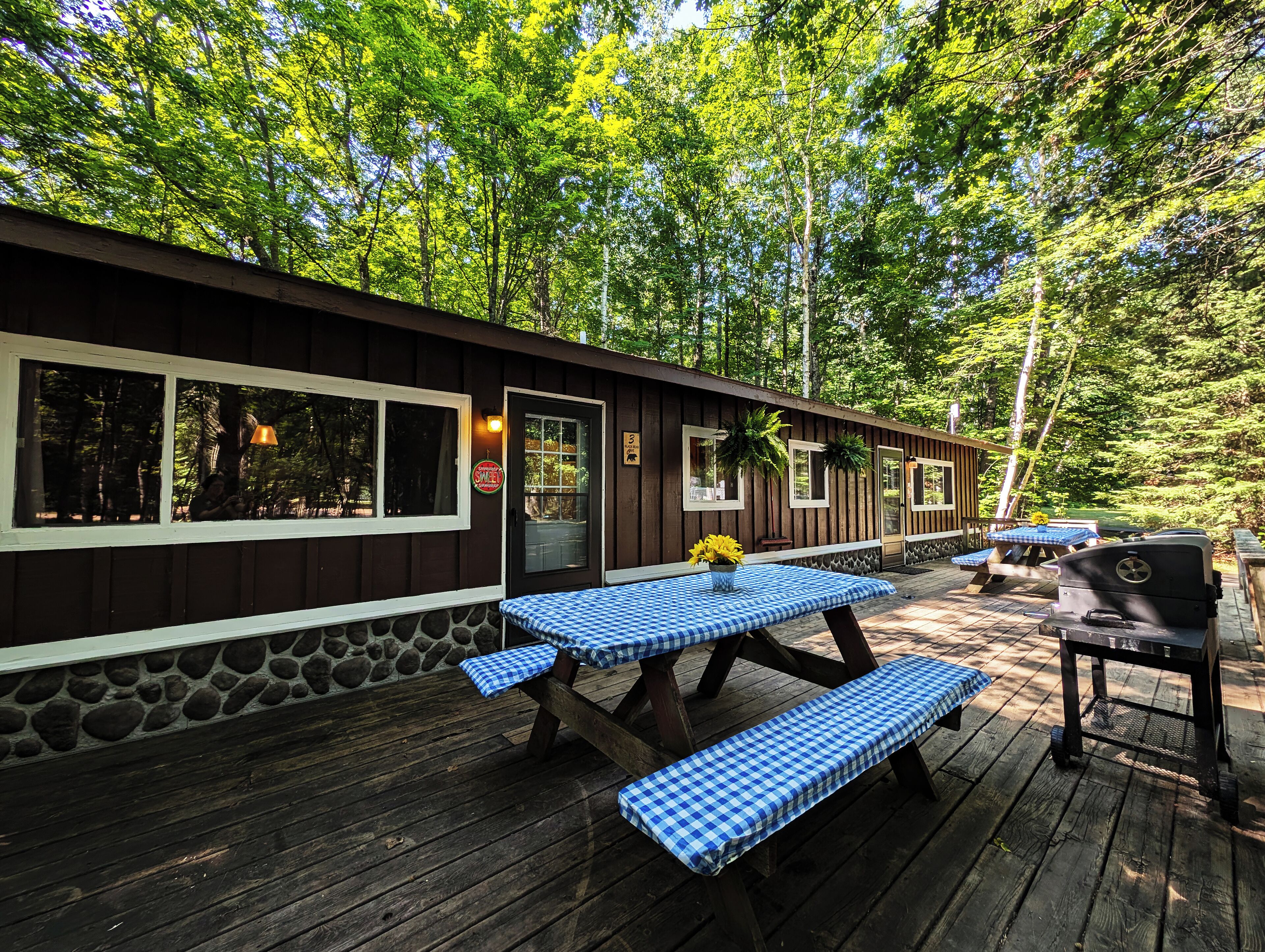 A wooden deck with picnic tables and a barbecue grill, surrounded by trees.