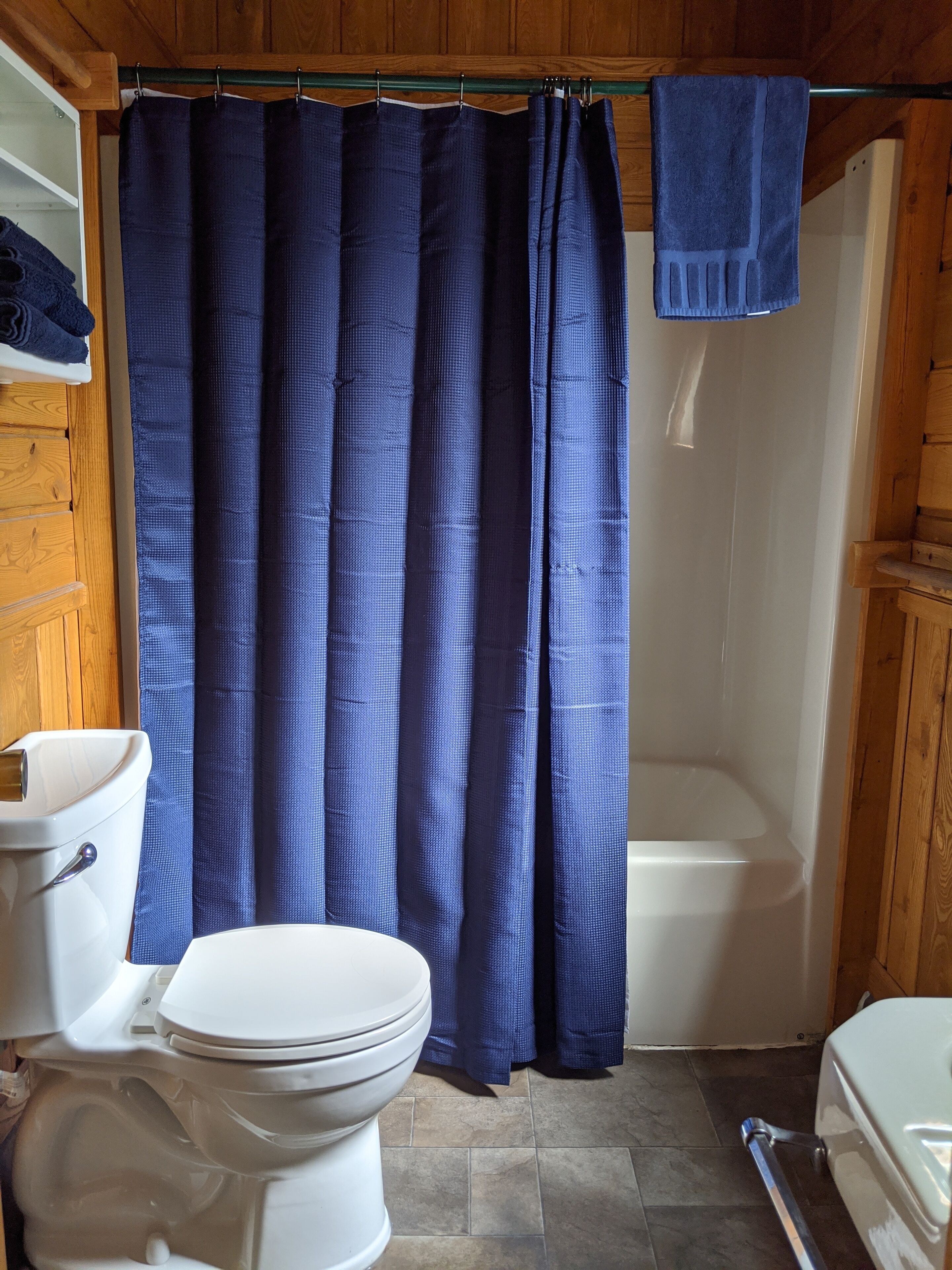 Une salle de bain avec des toilettes blanches, une baignoire et un rideau de douche.