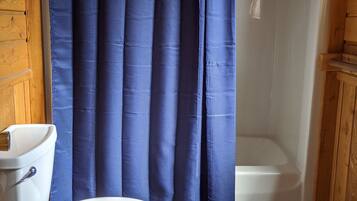 Une salle de bain avec des toilettes blanches, une baignoire et un rideau de douche.