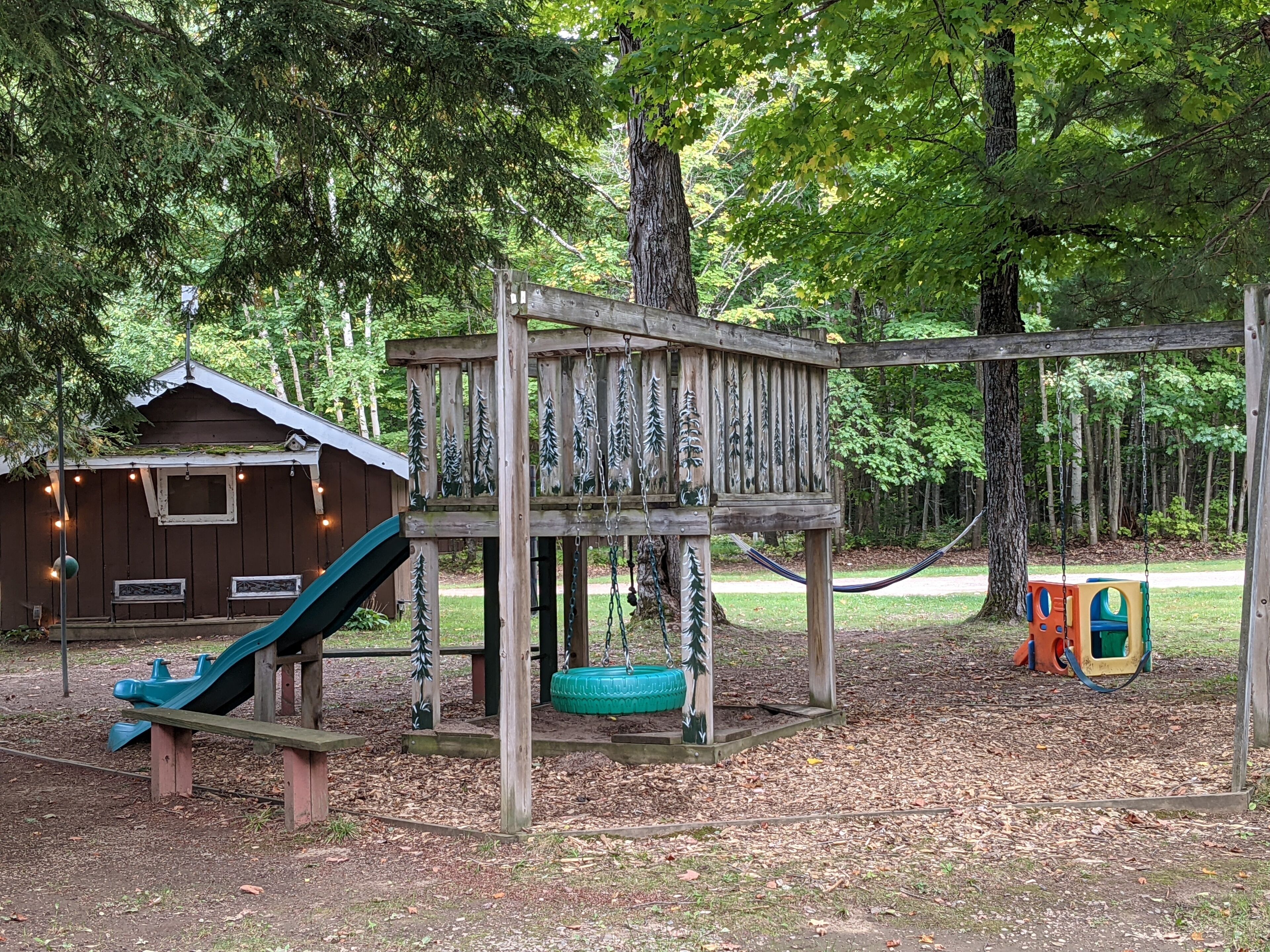 A wooden play structure with a slide and swings, surrounded by trees.