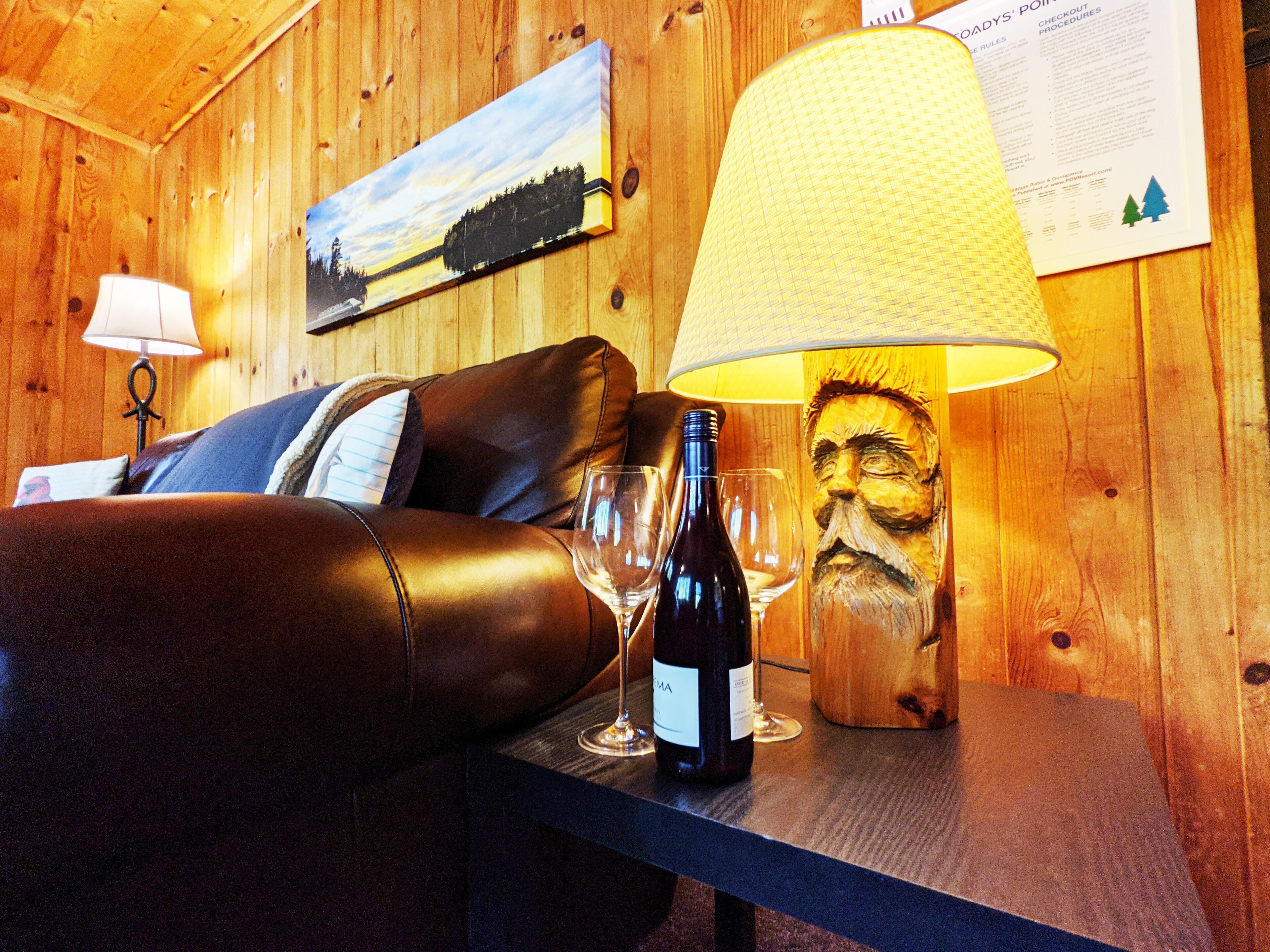 Un intérieur en bois avec un canapé en cuir, une table sur laquelle se trouvent une bouteille de vin et des verres, une lampe et un tableau accroché au mur.
