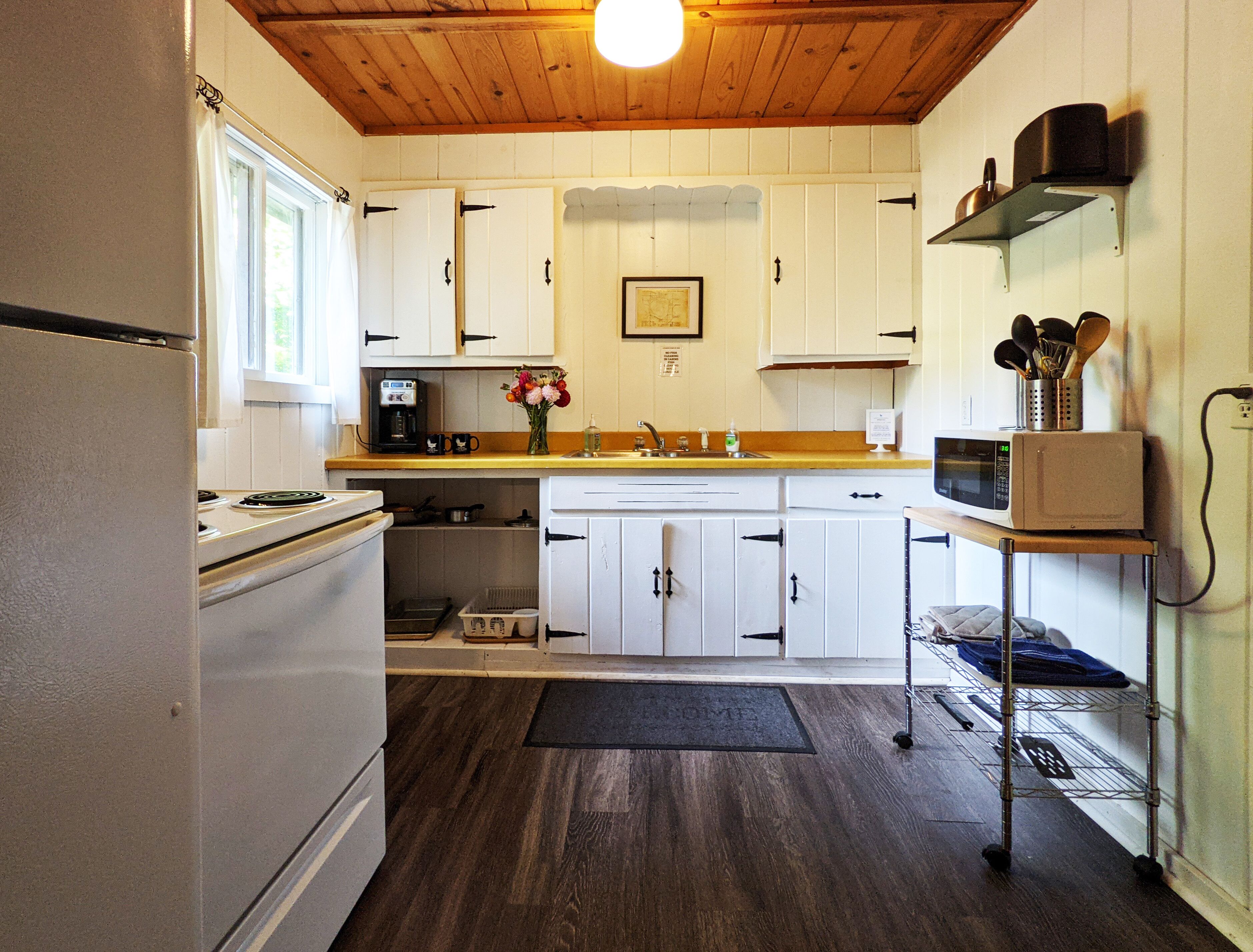 Cocina compacta con alacenas blancas, microondas, cafetera y un lavamanos pequeño.