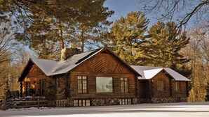 A log cabin with a stone foundation, large windows, and a snow-covered roof. - POV Lake Resort & Glamping Campground (Phelps)