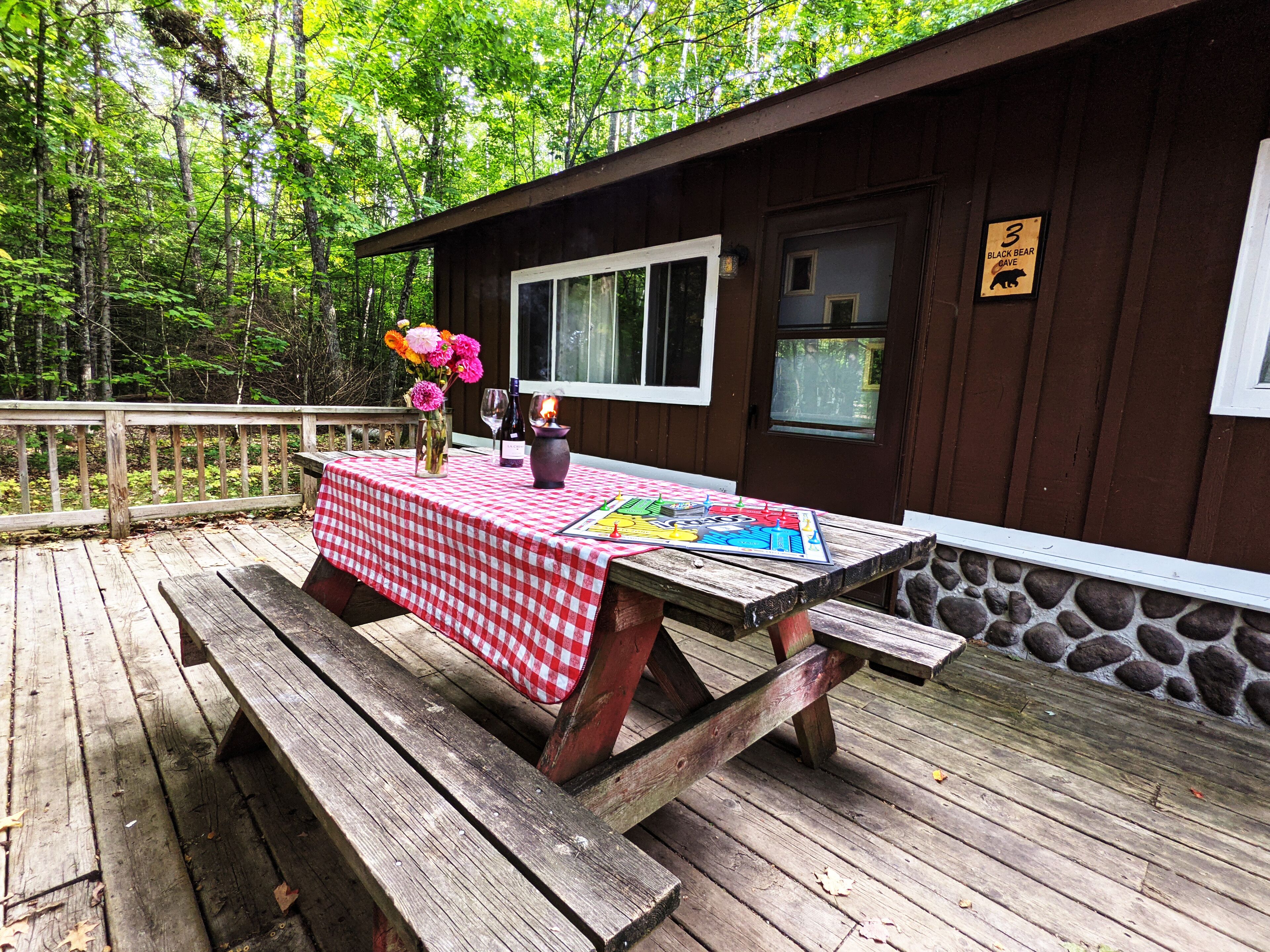A wooden deck with a picnic table set up, a vase with flowers, and a sign indicating a black bear cave nearby.