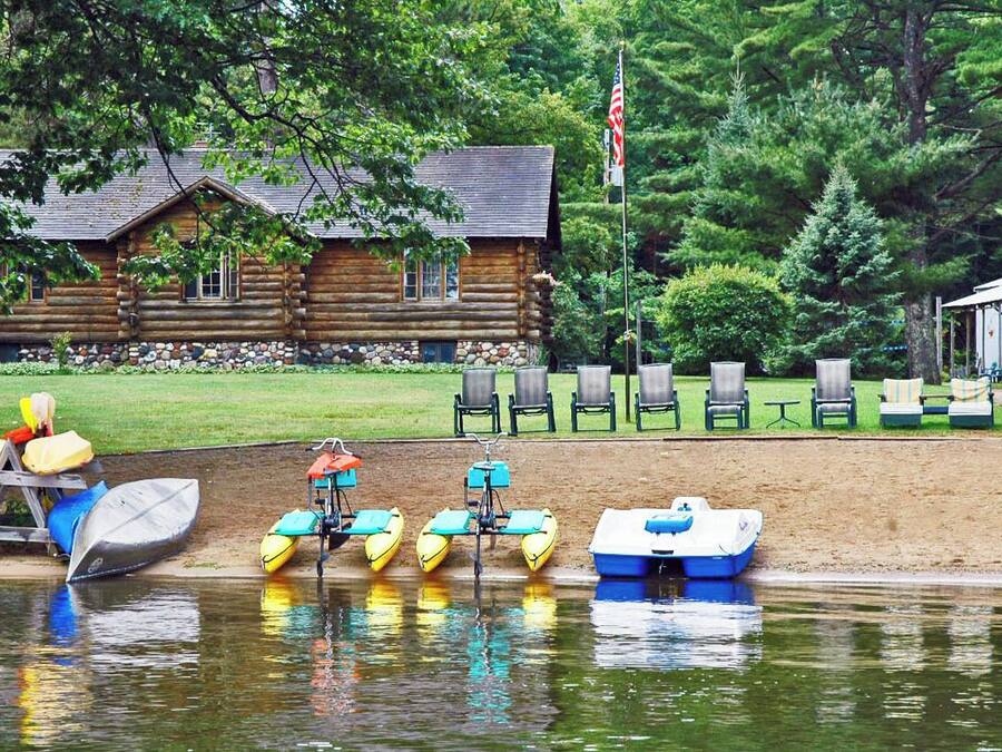 A log cabin with a dock, kayaks, and lounge chairs by a lake.