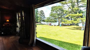 A room with a large window overlooking a grassy outdoor area with trees and a lake.