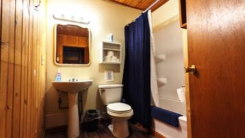 Un baño pequeño con piso de madera, un lavamanos, un inodoro, una ducha y un espejo.