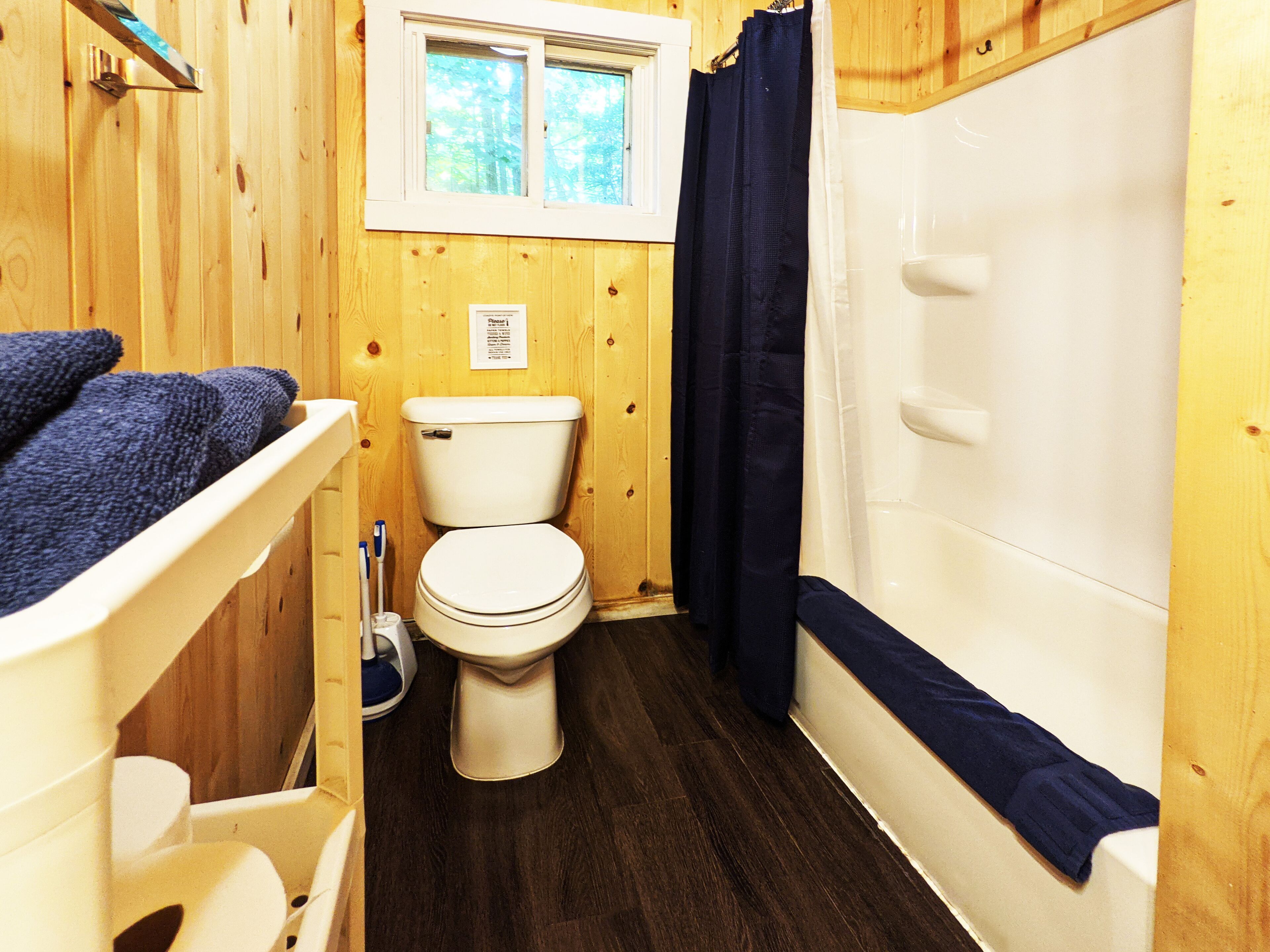 Baño de cabaña de madera con inodoro, bañera y ventana sobre el inodoro.