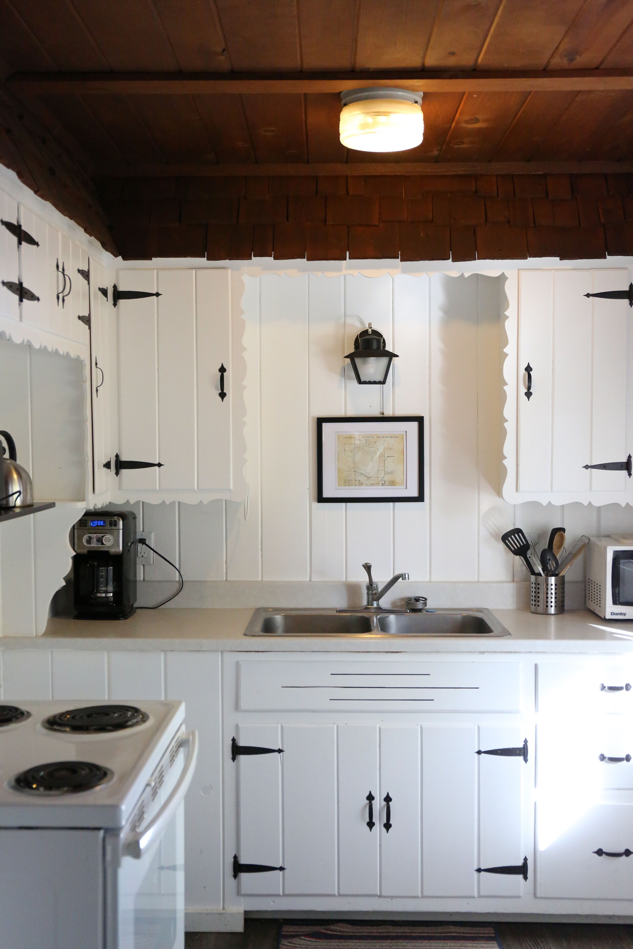 A kitchen with white cabinets, a stove, a sink, and a coffee maker.