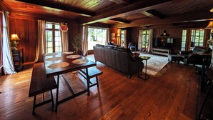 A spacious living room with a wooden ceiling, a large sofa, a television, and a dining area with a table and benches. - POV Lake Resort & Glamping Campground (Phelps)